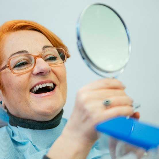 An older woman admiring her smile with a hand mirror