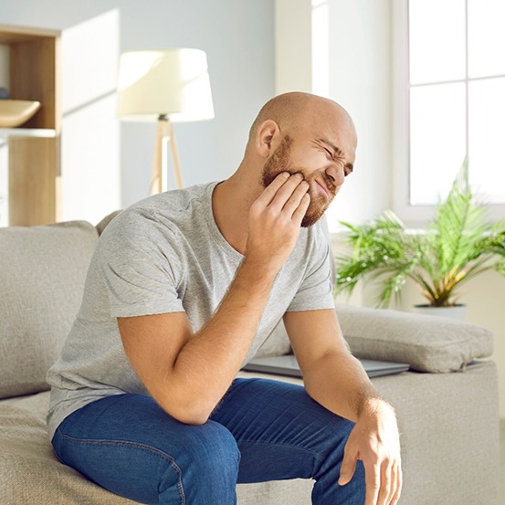 Man squinting in pain and holding his jaw