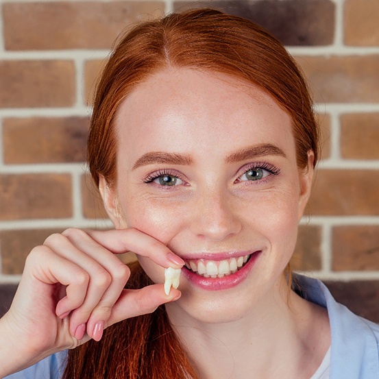 Woman with red hair holding extracted tooth