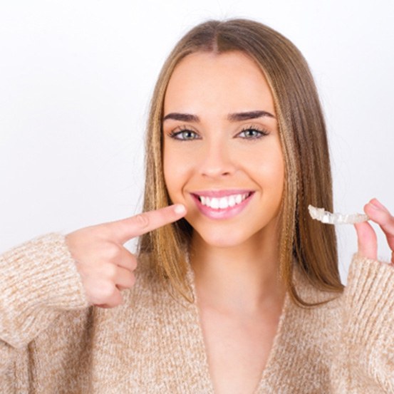 A smiling woman holding an Invisalign tray