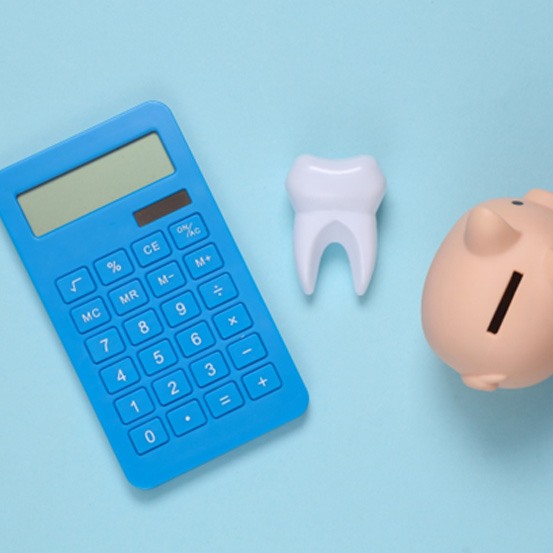 A calculator, model tooth, and piggy bank set against a blue background