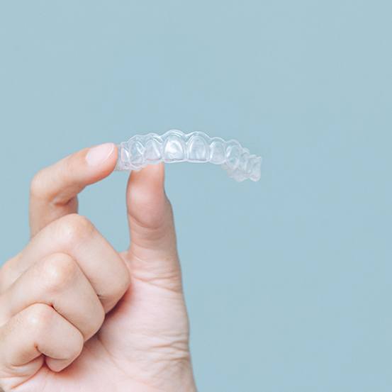 Patient holding Invisalign clear aligners against blue background