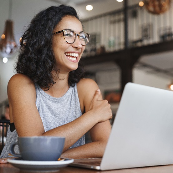 Woman with glasses smiling while working on laptop