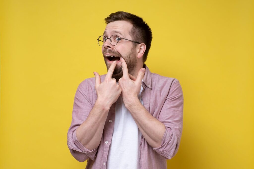 Man in glasses touching broken tooth with two fingers with yellow background