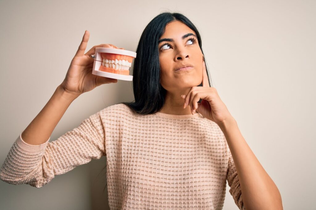 A thinking woman holding a model of teeth